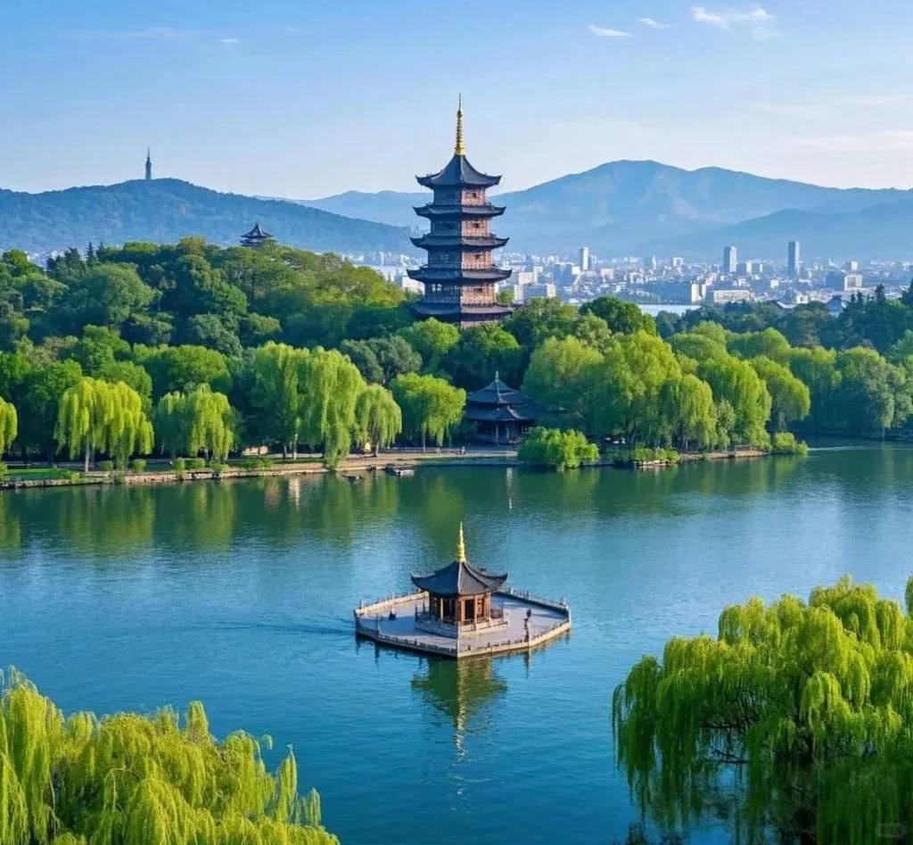 Panoramic view of Hangzhou West Lake in China, showing Leifeng Pagoda on a tree-covered hill, and a traditional pavilion on a small square island in the clear blue water. Lush green trees, including weeping willows, line the lake's edge, with distant mountains and a modern city skyline visible under a bright blue sky.