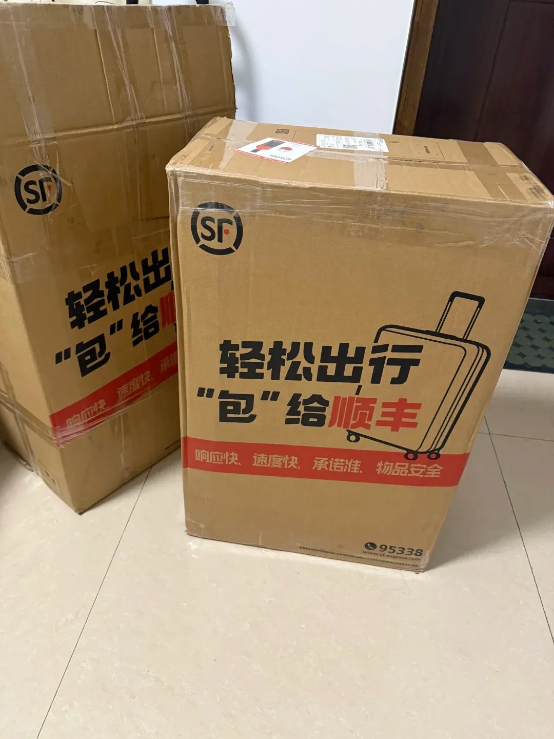 Two large, taped-up brown cardboard SF Express boxes featuring the SF logo, Chinese text about easy travel and luggage, and a graphic of a suitcase on a light-colored tiled floor.