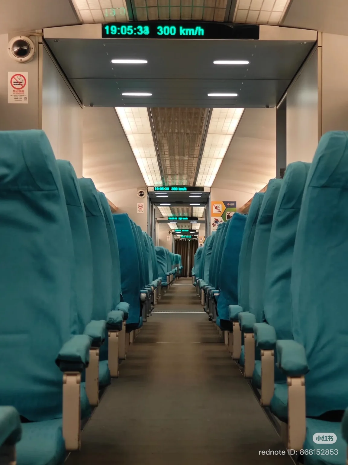 Interior of a high-speed train with rows of teal seats on either side of a central aisle. A digital display at the front shows the time as '19:05:33' and the speed as '300 km/h'. Lighting panels are visible on the ceiling.