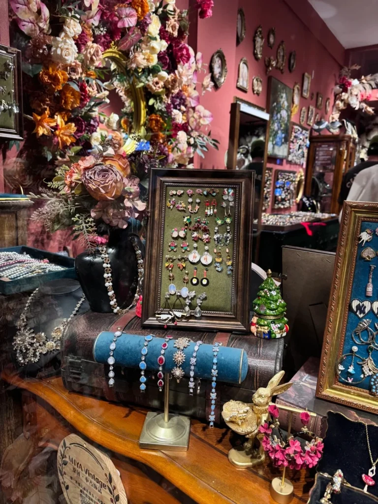 A display of vintage jewelry including bracelets and earrings, alongside a large floral arrangement and decorative items like a miniature Christmas tree and a golden rabbit figurine.