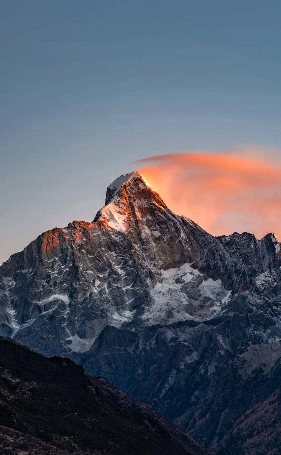 A majestic, snow-capped mountain peak illuminated by the golden light of sunrise, with a vibrant orange cloud formation draped over its summit.