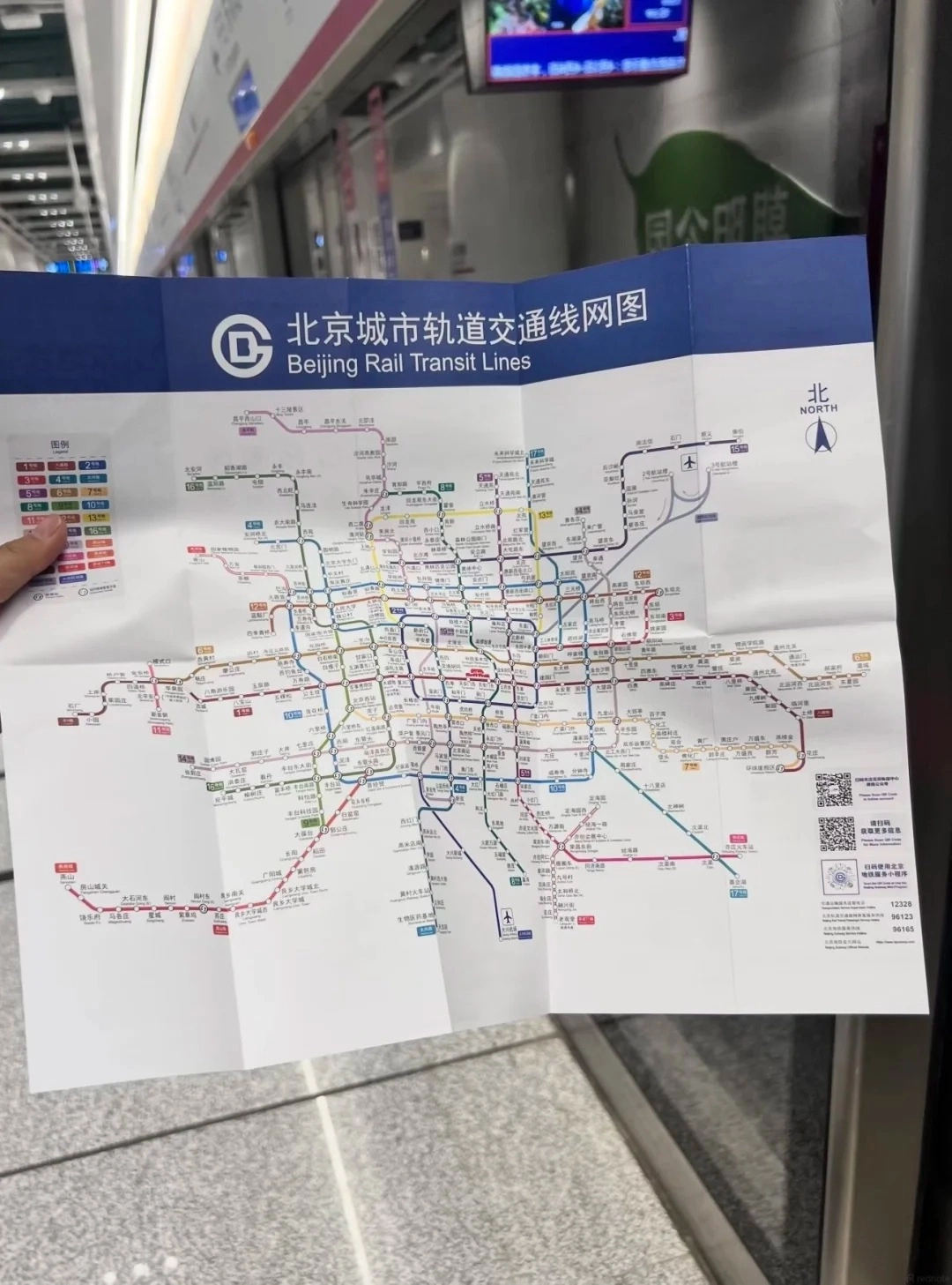 A person holding a folded Beijing Rail Transit Lines map inside a subway station platform.
