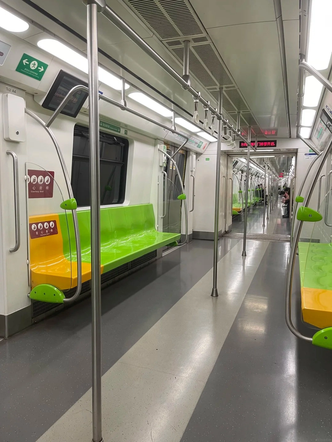 An empty subway train interior with green and yellow seats, silver poles, overhead hand straps, and a gray floor.
