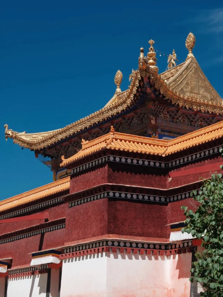 The golden roof and upper facade of a traditional Tibetan monastery with red walls and white trim, under a clear blue sky.